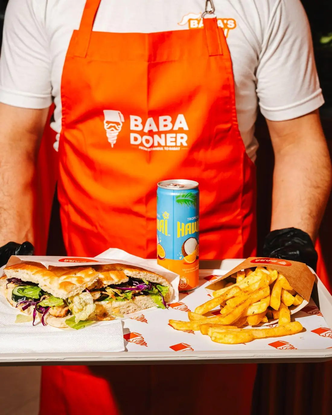 Staff member in a branded apron holding a full tray