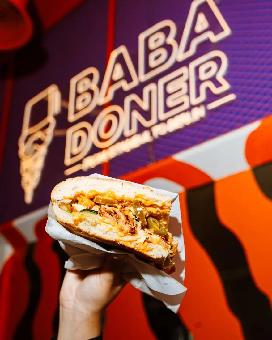 Sandwich held up in front of the Baba Doner neon logo