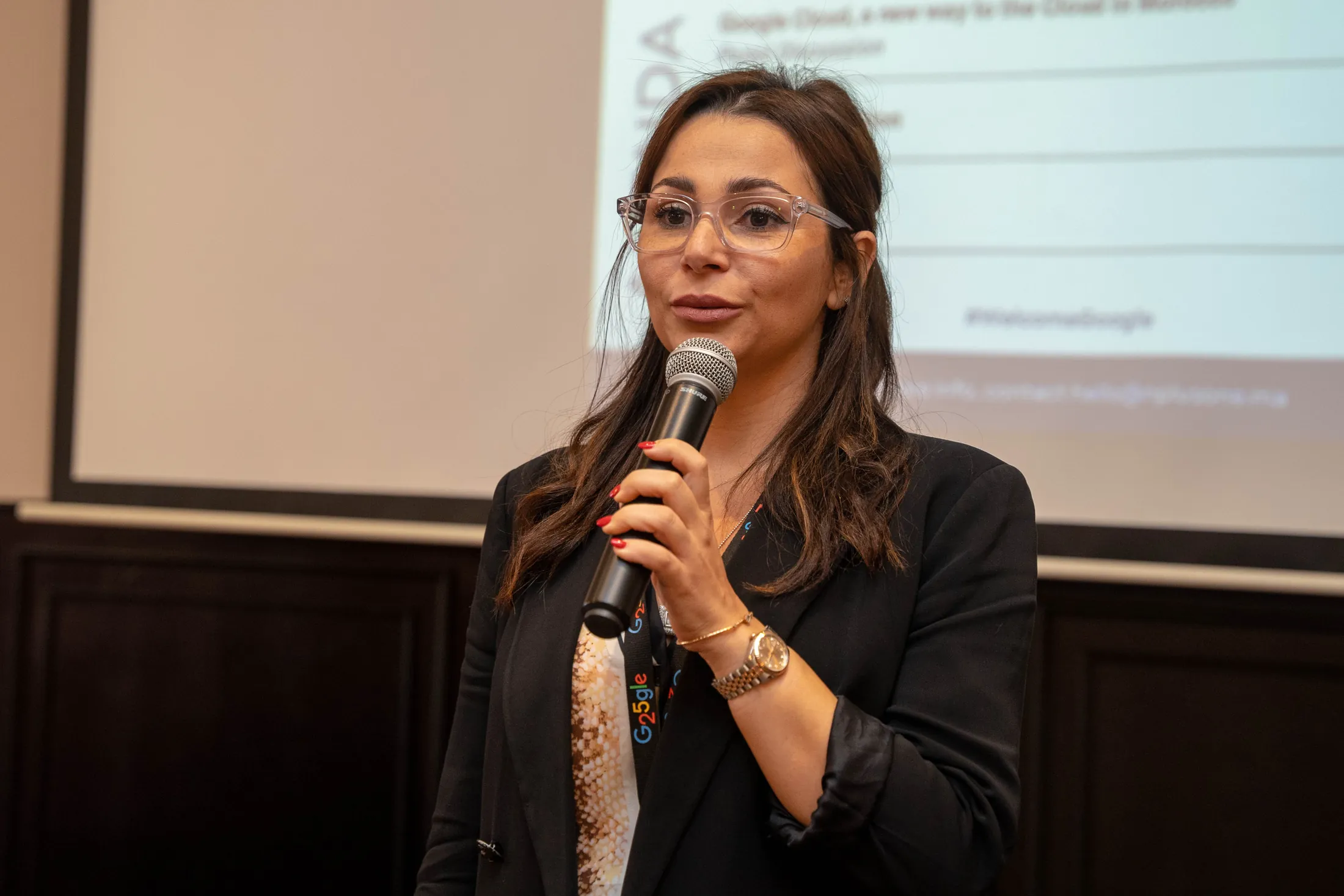Speaker presenting with a microphone in front of the agenda screen