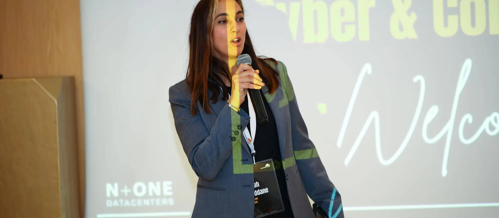 Speaker on stage in front of the Cyber & Connect welcome screen at an N+ONE event
